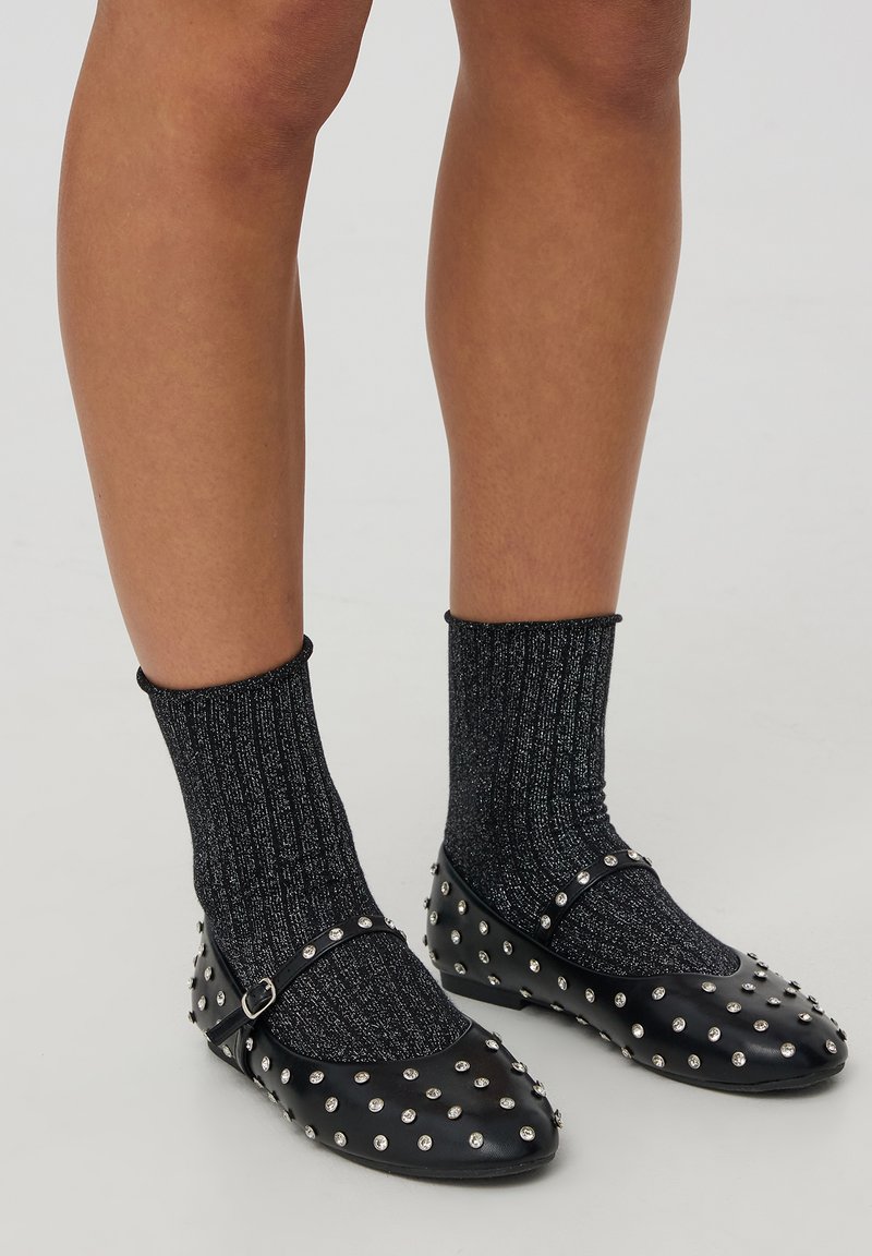 Ballerine nere con borchie, dotate di una cinghia, indossate con calze nere a coste scintillanti. Le ballerine sono decorate con borchie argento per un tocco in più.