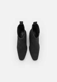 Svarta anklarstövlar med spetsig tåform, tillverkade av ett strukturerat mockamaterial, med en dragflik på hälen och ribbade detaljer.