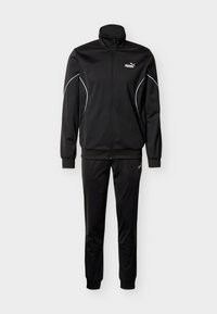 Μαύρο φόρμα από λείο, ελαφρύ ύφασμα. Διαθέτει ψηλό γιακά, κλείσιμο με φερμουάρ και αντίθετα λευκά ραφές κατά μήκος των μανικιών και του παντελονιού.