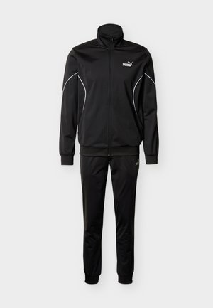 Tuta nera realizzata in tessuto liscio e leggero. Presenta un colletto alto, chiusura con cerniera e cuciture bianche a contrasto lungo le maniche e i pantaloni.