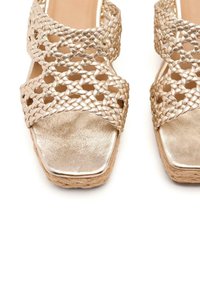 Sandali in faux leather dorato intrecciato con punta quadrata, dotati di cinturini incrociati e suola naturale texture.
