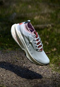 Botte de course en gris clair, avec une tige texturée, des accents roses, un col rembourré et une semelle intermédiaire mouchetée. Semelle extérieure en caoutchouc stabilisante.