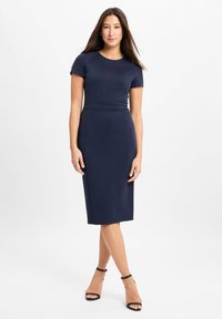 Navyblaues, tailliertes Kleid mit kurzen Ärmeln, rundem Ausschnitt und Nahtdetails. Getragen mit schwarzen Ankle-Strap-High Heels. Glattes, elastisches Material.