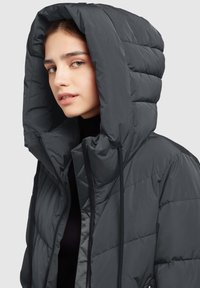 Hall puffer-jakk suurte kapuutsi disaini ja tikitud tekstuuriga. Omab musti nöörke ja esi tõmblukk. Kerge materjal.