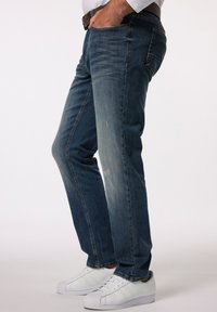 Vaqueros de mezclilla en azul oscuro con un acabado ligeramente desgastado, presentan un corte recto, sutiles desgastes y se combinan con zapatillas blancas.