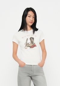 Hvit bomulls t-skjorte med rund hals og korte ermer. Har et grafisk motiv av en hestesko og roser i dempede farger. Kombinert med lysegrå jeans.
