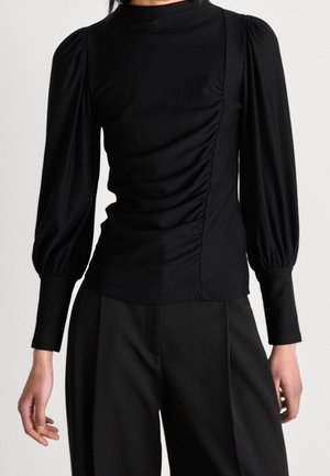 Top nero a maniche lunghe con spalle a sbuffo, dettaglio arricciato sui lati e collo alto. Realizzato in un tessuto liscio ed elasticizzato.