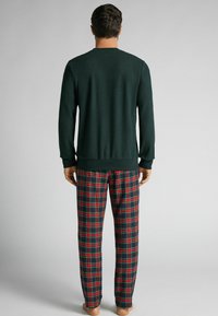 Pull col rond vert foncé, associé à un pantalon de pyjama à carreaux rouge et bleu. Le tissu semble doux avec des poignets et une taille côtelés.