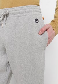 Grijze sweatpants gemaakt van zacht materiaal, met een elastische tailleband met trekkoorden, zijzakken en een geborduurd logo.