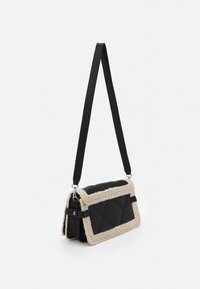 Svart läder crossbody-väska med cremefärgad konstpäls, quiltat mönster, justerbar axelrem och silverdetaljer.