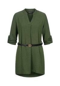 Tunique verte à manches longues avec col en V, manches retroussées avec pattes boutonnées et ceinture noire fine avec boucle dorée double anneau à la taille.
