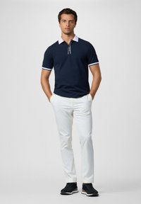 Námornícky polo tričko s bielym golierom a manžetami, v kombinácii s bielymi nohavicami a čiernymi teniskami. Minimalistický dizajn, krátke rukávy a detail so zipsom.