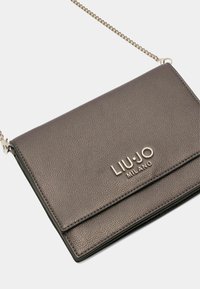 Šedá kožená crossbody taška s texturovaným povrchem, vybavená stříbrným řetízkem na nošení a embosovaným logem na přední straně.