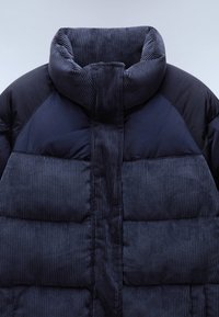 Námořnická pufrová bunda s žebrovaným kordovým límcem a panely. Měkká, texturovaná látka s prošívaným vzorem a nadýchanými sekcemi.