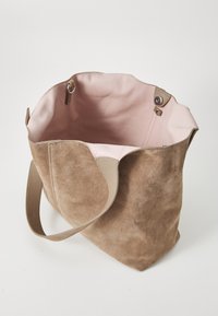 Borsa tote in suede beige con finitura strutturata, dotata di un interno rosa chiaro, due chiusure a scatto superiori e una larga tracolla.