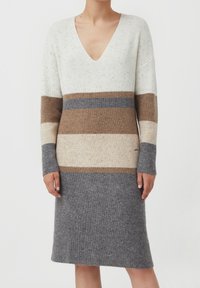 Sukienka dzianinowa z dekoltem w serek, ozdobiona poziomymi paskami w kolorach kremowym, beżowym, brązowym i szarym. Dzianina o fakturze z delikatnym efektem cętkowania.