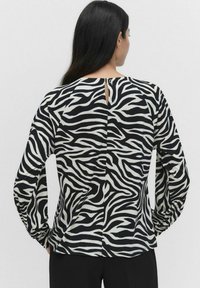 Zebra print -mustavalkoinen paita, jossa on pitkät hihat, pehmeä kangas ja avainreikäyksityiskohta takana. Muotoiltu malli, jossa on hienovarainen kiilto.