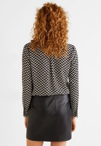 Bagudsigten af en person iført en bluse med sort og hvidt mønster og lange ærmer, kombineret med en tætsiddende sort læder-miniskirt.