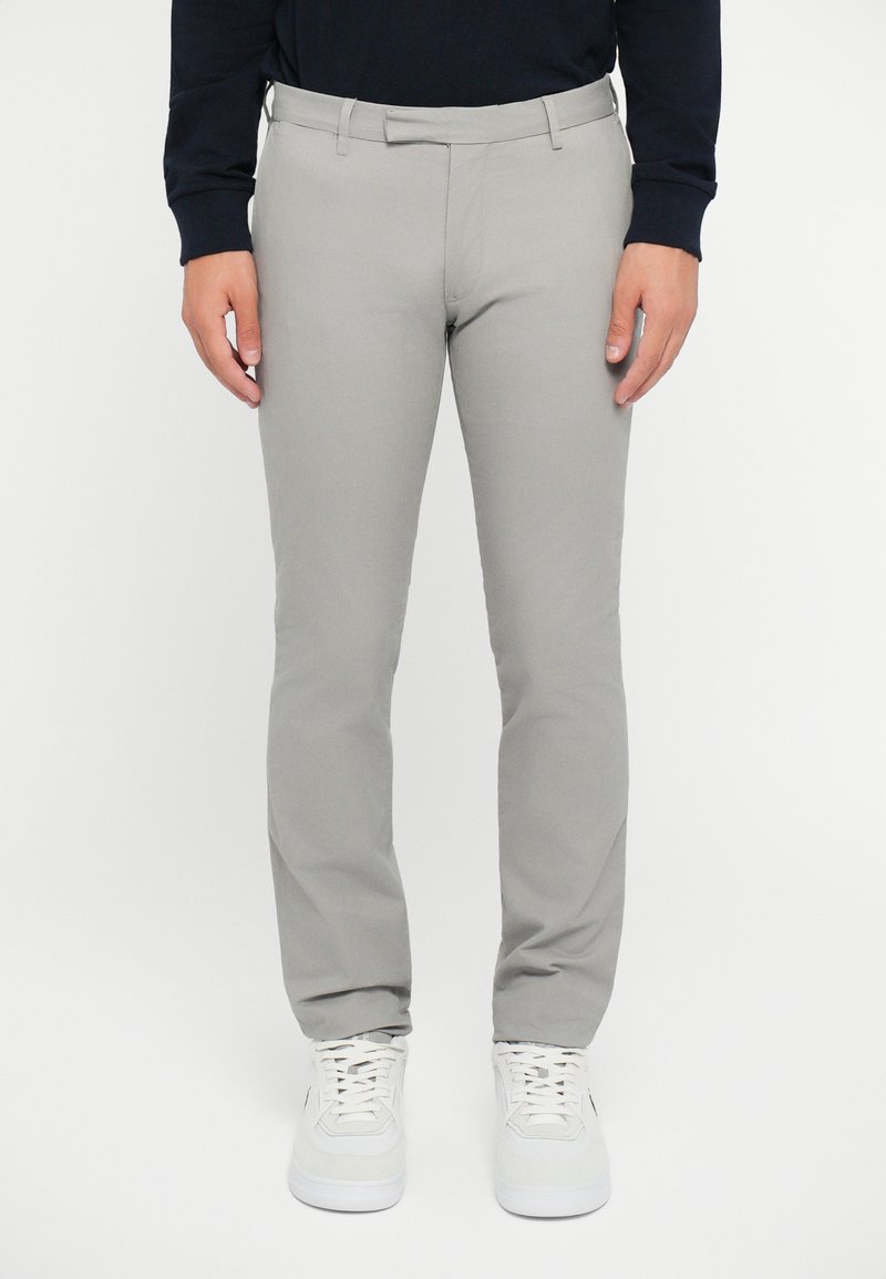 Pantalones de corte ajustado en un gris claro con una textura suave y elegante. Cuentan con una cinturilla estándar y bolsillos laterales, combinados con zapatillas blancas.