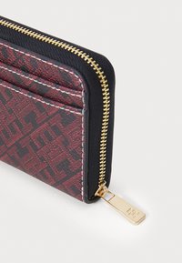 Cardholder in red and black with a textured pattern, gold zipper, and a rectangular shape. Features slots for cards and a zip closure.