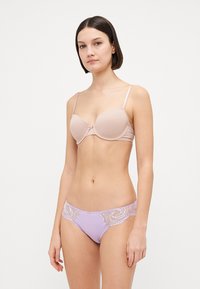 Lys beige polstret bh med justerbare stropper, sammen med lavendelfargede truser med blondekant som har dekorative mønstre på siden.