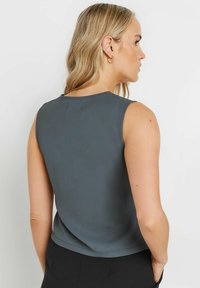 Grå ärmlös topp med rundad halsringning och mjuk textur, med en enkel design och rena linjer på baksidan.