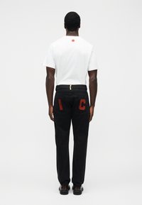 Μαύροι φόρμες με κόκκινες μπαλώματα "I" και "C" στις πίσω τσέπες. Λευκό μπλουζάκι με κυκλικό λογότυπο στο πάνω μέρος της πλάτης. Απλή υφή.