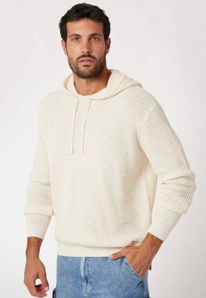 Crèmekleurige gebreide hoodie met een gestructureerd patroon, verstelbare trekkoord en geribde manchetten en zoom, gecombineerd met lichte denim shorts.