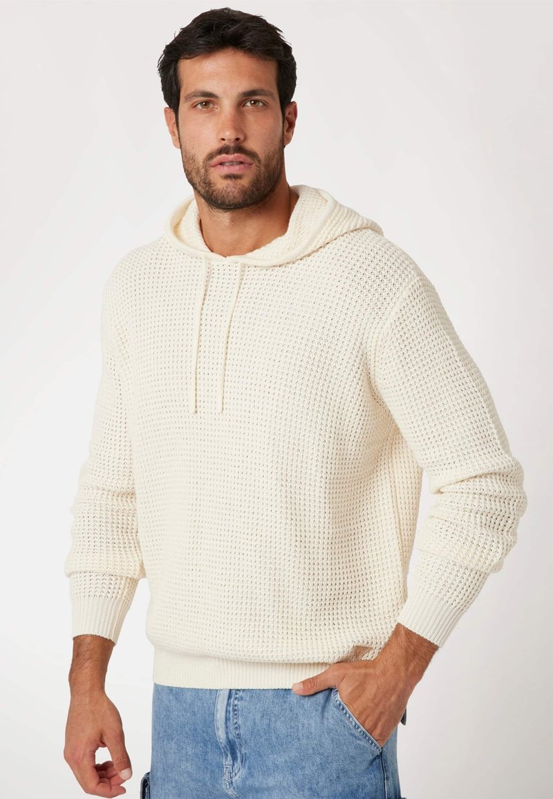 Crèmekleurige gebreide hoodie met een gestructureerd patroon, verstelbare trekkoord en geribde manchetten en zoom, gecombineerd met lichte denim shorts.