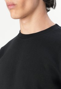 Sudadera de algodón negra con cuello redondo y puños acanalados. Textura suave con un diseño simple y minimalista. Sin patrones ni acentos.