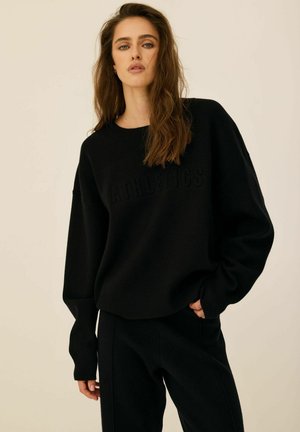 Czarna, oversize bluza z nadrukiem "ATHLETICS", ściągacze na nadgarstkach i okrągły dekolt; zestawiona z dopasowanymi ciemnymi spodniami.