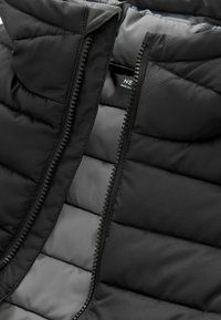 Gilet en duvet noir avec une fermeture éclair sur le devant, présentant un design matelassé et une texture lisse et brillante. Doublure intérieure en tissu gris.