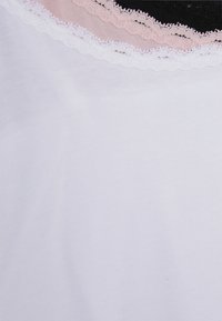 Canottiera bianca realizzata in un morbido tessuto di cotone. Il collo presenta strati di pizzo in rosa, bianco e nero, creando un bordo testurizzato.