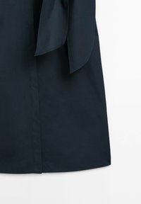 Tissu de vêtement bleu marine foncé avec une couture visible et deux panneaux de tissu effilés suspendus sur un fond blanc.