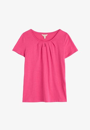 Rāvas rokas piedurkņu rozā T-kreklā, izgatavots no mīkstas auduma, ar apaļu dekoltē un pleiti zem dekoltē. Gluda tekstūra, brīvs griezums.