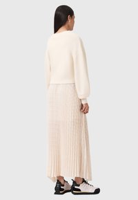 Maglione chiaro in crema con maniche lunghe e polsini a costine, abbinato a una gonna trasparente plissettata fino al pavimento di un delicato rosa pallido e sneakers in bianco e nero.