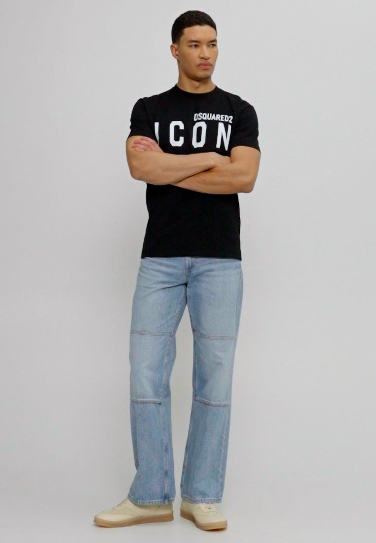 Черен тениска с бяло изписано "ICON" отпред, комбинирана с светлосини дънки с панели и маратонки с текстурирана подметка.