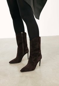 Botines de ante burdeos oscuros con punta afilada, tacones altos de aguja y cremalleras laterales visibles. Diseño simple y elegante.