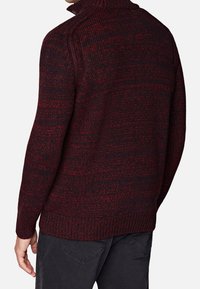 Pull en tricot dans des tons rouge foncé et noir. Il présente un col montant et des poignets côtelés. La vue de dos montre un motif en tricot épais et texturé.