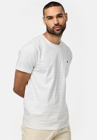 Weißes T-Shirt mit kurzen Ärmeln, dünnen, bunten horizontalen Streifen und einer kleinen Brusttasche. Weiches Material, Rundhalsdesign.