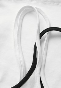 Gros plan de bandes élastiques blanches et noires sur un fond en tissu blanc, montrant la texture et les détails de la couture.