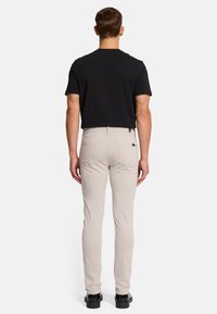Beige slim-fit broek met een platte tailleband, twee achterzakken en een klein merketiket. Draag met een zwarte shirt met korte mouwen.