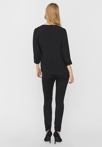 Schwarzes Oberteil mit Dreiviertelärmeln, Rundhalsausschnitt und Raffung an den Ärmeln, kombiniert mit schwarzen, schmalen Hosen und High Heels.