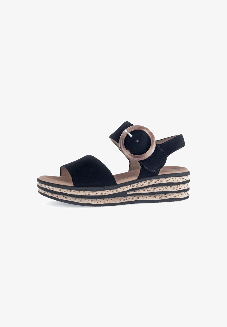 Black sandal with a round wooden accent and adjustable strap. Features a textured, layered sole with black and light brown stripes.