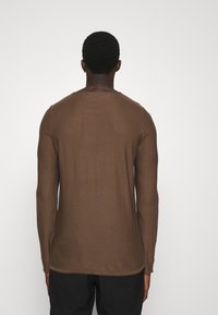 Ruskea pitkähiha paita pehmeästä kankaasta, jossa pyöreä pääntie ja suora leikkuu, resorireunuksilla hihansuissa ja helmassa.