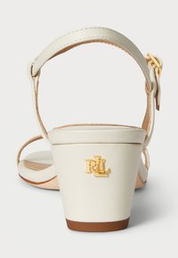 Kreemivärvi kontsad, millel on lai rihm ja pahkluu pannal. Märkimisväärne kuldne "RL" embleem kontsal, tekstureeritud tallaga.