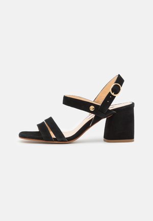 Sandalias de tacón alto de ante negro con dos tiras frontales, una tira en el tobillo y una hebilla redonda. Acabado texturizado con tacón bloque sólido.