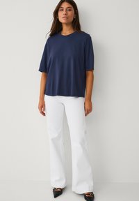 Navyblauw T-shirt met korte mouwen en een losse pasvorm, gecombineerd met witte flared broek en zwarte schoenen met spitse neus en een gespsluiting.
