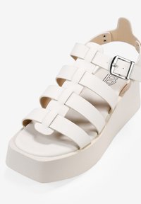 Sandalias de plataforma blancas con múltiples correas anchas y planas, y una hebilla plateada. Textura suave y suela sólida en forma de cuña.