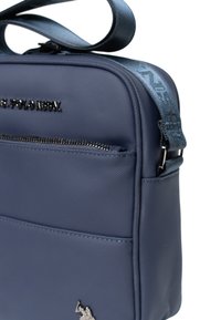Granatowa syntetyczna torba o gładkiej teksturze, z przednią kieszenią na zamek, logo oraz wzorzystym regulowanym paskiem.